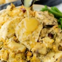 A pile of stuffing on a plate topped with cooked chicken with gravy being drizzled on top.