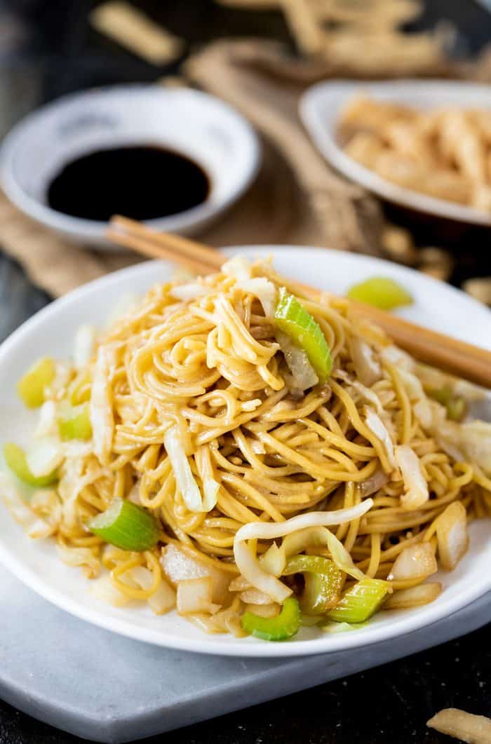 white plate filled with panda express chow mein with chopsticks and soy sauce in the background.