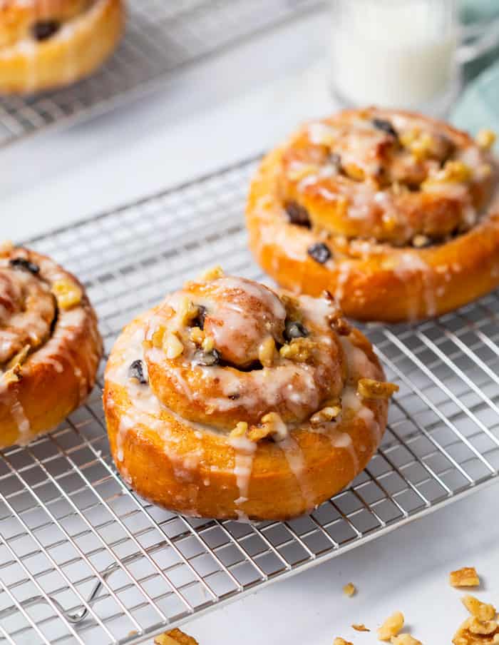 Homemade cinnamon rolls on a wire rack topping with raisins and white icing.
