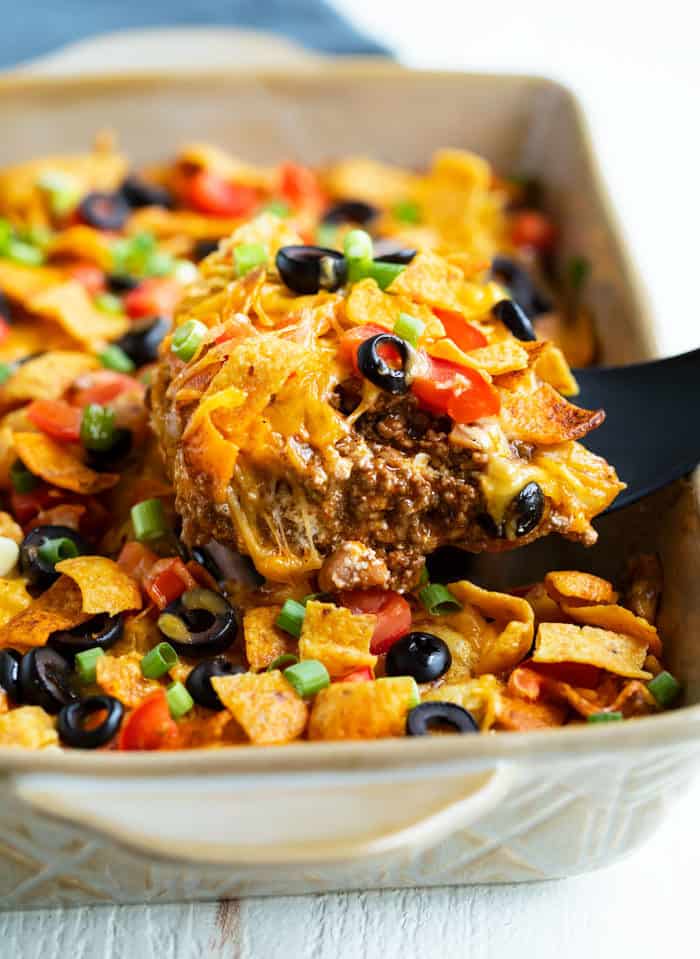 This Taco Casserole is easy to make ahead of time and bake later! It's loaded with juicy ground beef and your favorite Mexican toppings for a perfect weeknight dinner! #doritos #fritos #recipe #mexicanrecipes #easydinnerideas #familydinner #groundbeefrecipes Taco Casserole being scooped out of a casserole dish with a spatula.