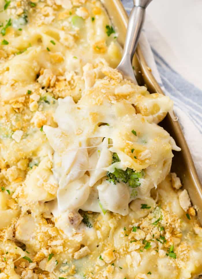 A spoon scooping up Chicken Alfredo Bake from a casserole dish.