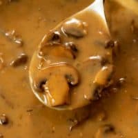 A spoon full of creamy mushroom gravy from a skillet.