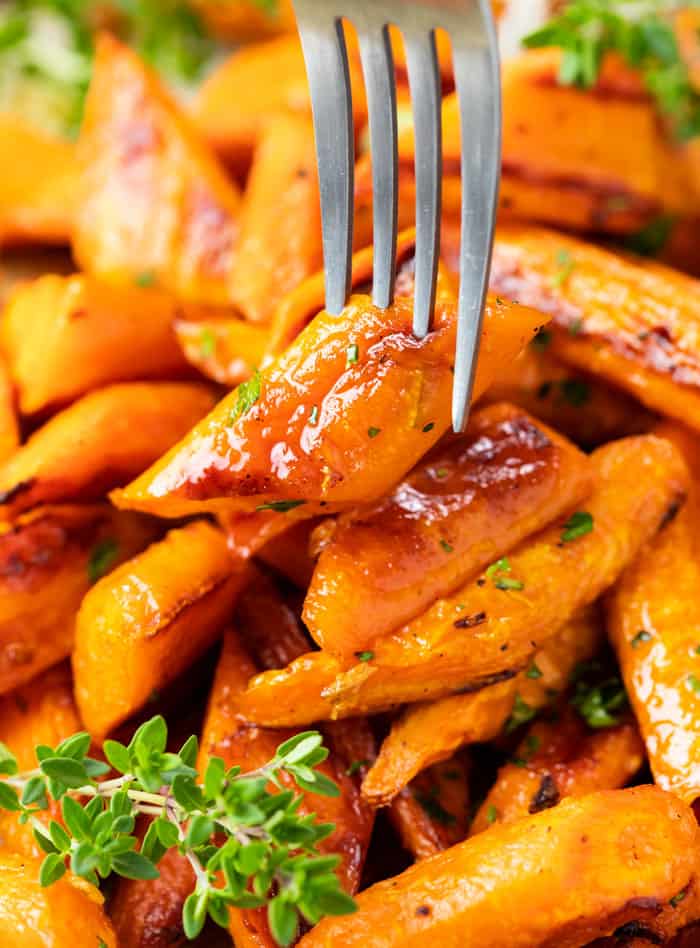 A fork picking up a roasted carrot from a pile.
