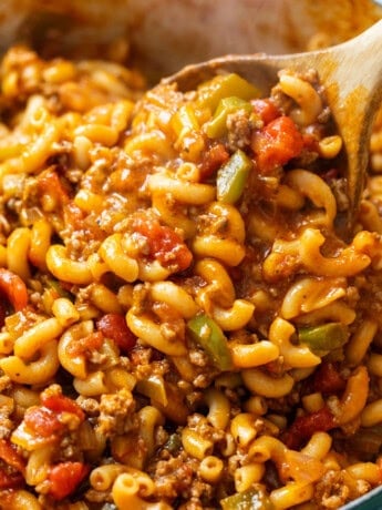A wooden spoon stirring a pot of hot American Chop Suey.