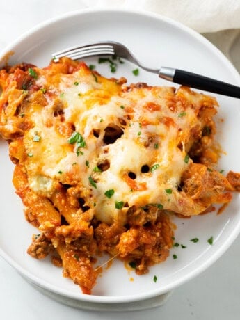 Cheesy Pasta Bake on top of a white plate with a fork and fresh parsley.