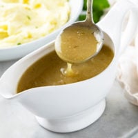 A ladle scooping chicken gravy up from a gravy boat.