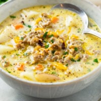 A bowl of creamy sausage potato soup topped with melted cheese.