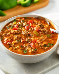 A bowl of Stuffed Pepper Soup with a spoon in it and bell peppers in the background.