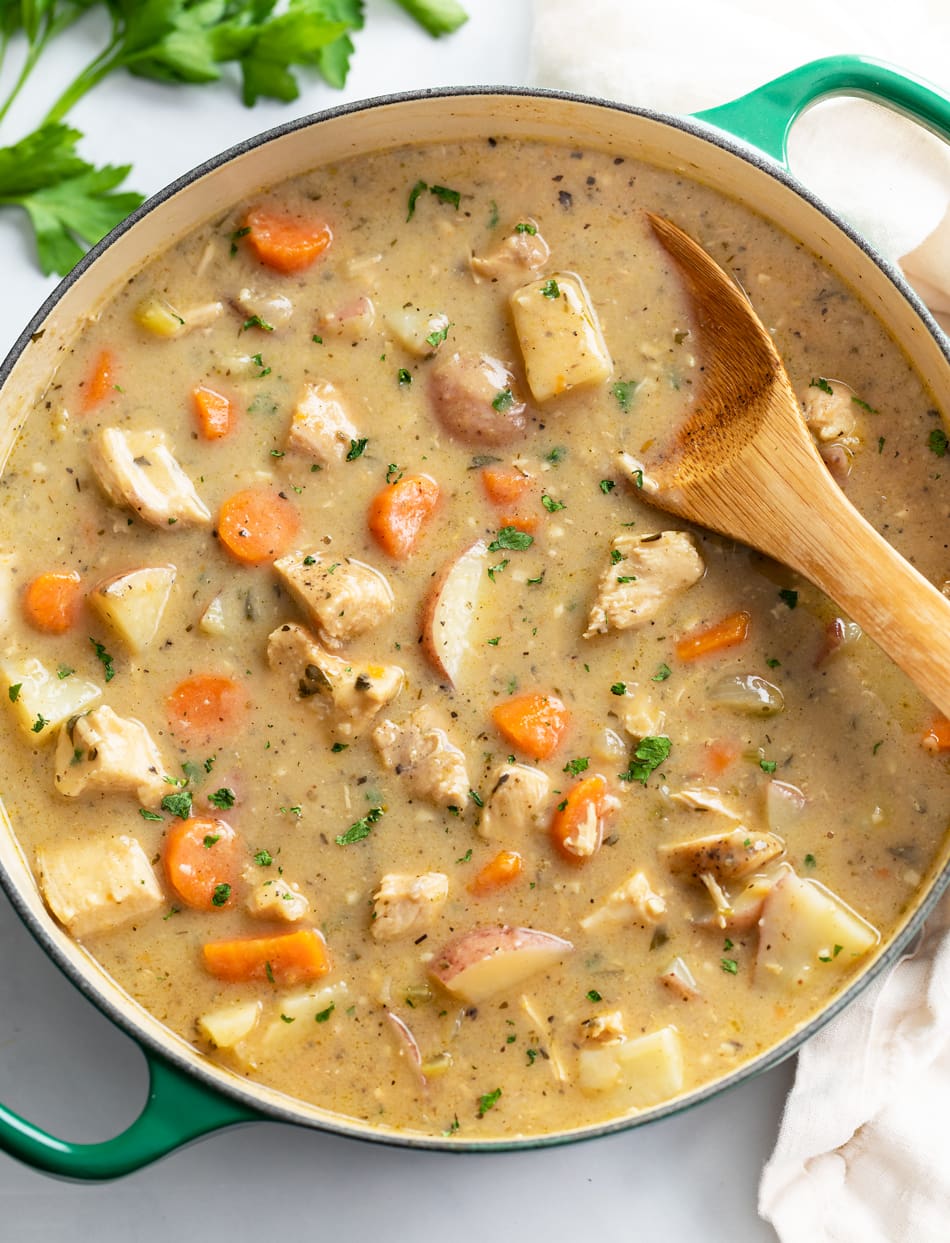 A Dutch oven filled with Chicken Stew with a wooden spoon in it.