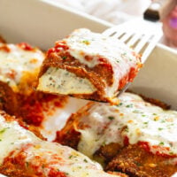 Eggplant Rollatini with ricotta filling being pulled up from a casserole dish by a spatula.