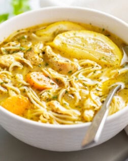 Lemon Chicken Soup in a white bowl with fresh lemon slices and a spoon on the side.