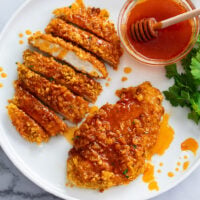 A white plate with crispy Hot Honey Chicken with sauce drizzled on top.