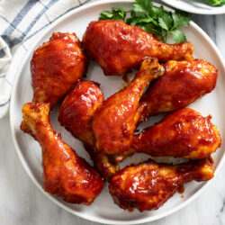 A white plate of Baked BBQ Chicken with parsley on the side.
