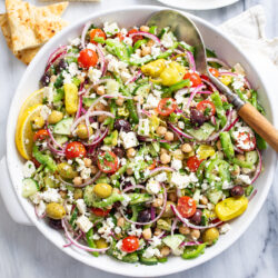 Greek Salad in a white bowl with vegetables, chickpeas, dressing, and feta.