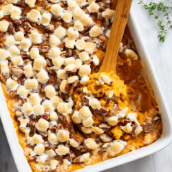 A wooden spoon scooping up sweet potato casserole from a baking dish.