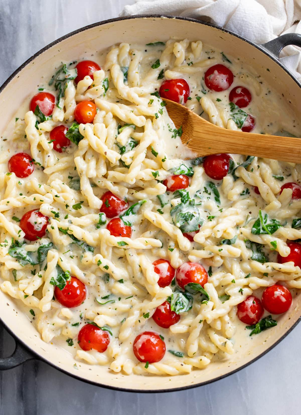 Boursin Pasta with a creamy herb sauce, spinach, and tomatoes in a skillet with a wooden spoon on the side.