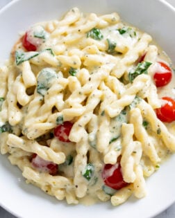 Creamy Boursin Pasta with an herb cream sauce, spinach, and tomatoes in a white bowl.