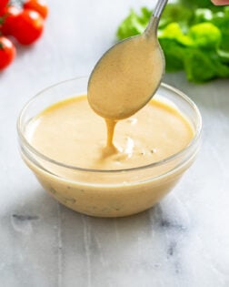 A spoon scooping out Big Mac Sauce from a small glass bowl with lettuce and tomatoes in the background.